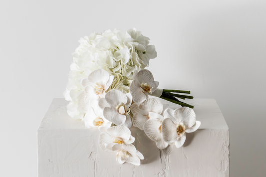 Artificial bridal white rose and orchid floral bouquet positioned elegantly on a textured plinth.