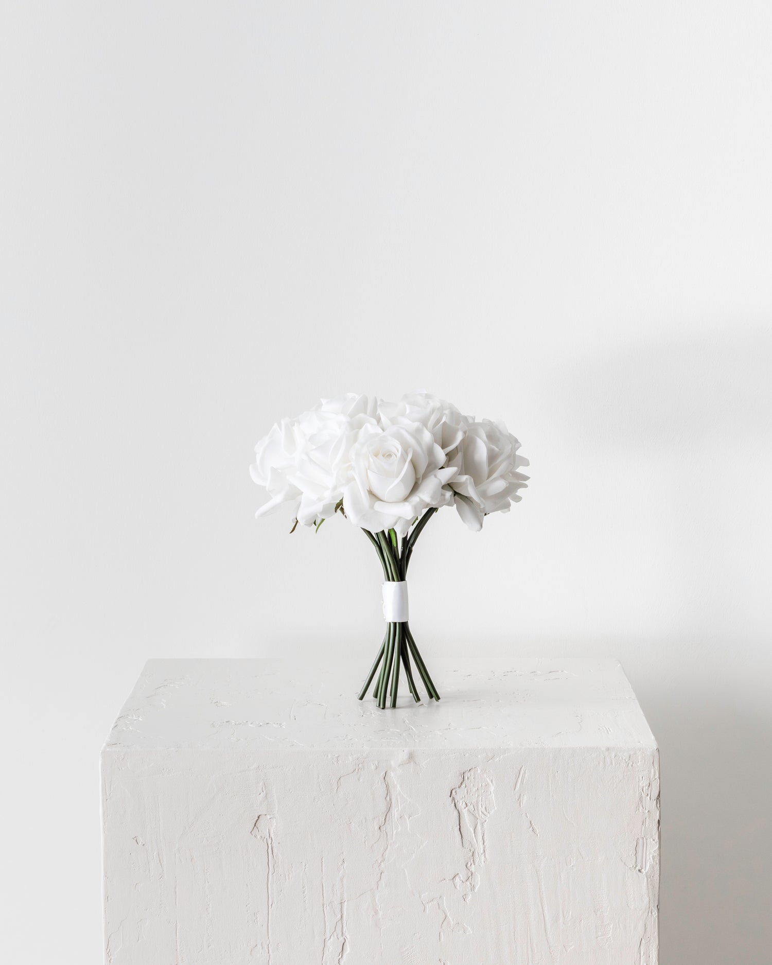 Elegant white rose bridal bouquet with real-touch petals displayed on a plinth, perfect for weddings and special occasions.