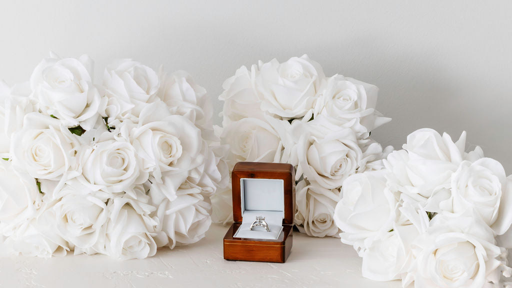 Three sizes of real-touch white rose bridal bouquets and an engagement ring in a wooden box elegantly arranged on a plinth.
