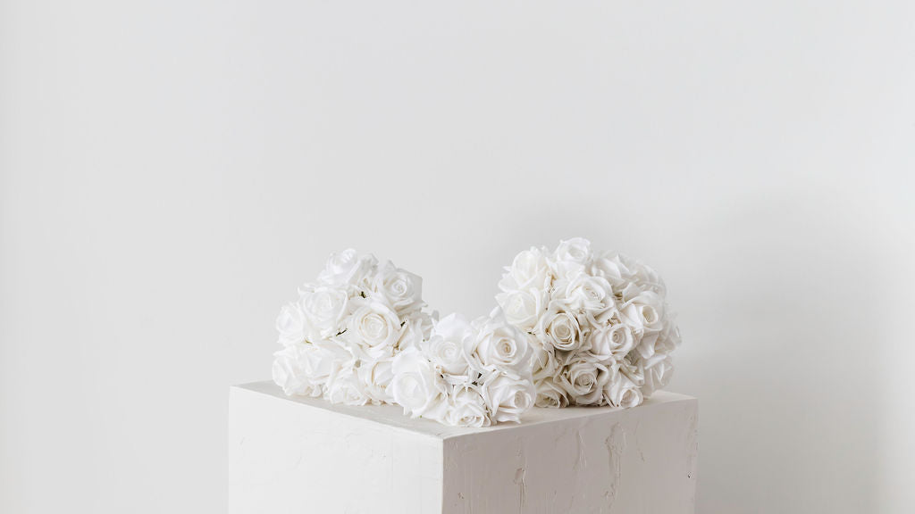 Three sizes of real-touch white rose bridal bouquets elegantly arranged on a plinth, showcasing their beauty.