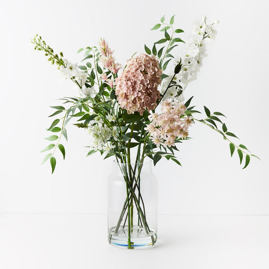 Pink hydrangea and delphinium floral arrangement in a tall glass vase